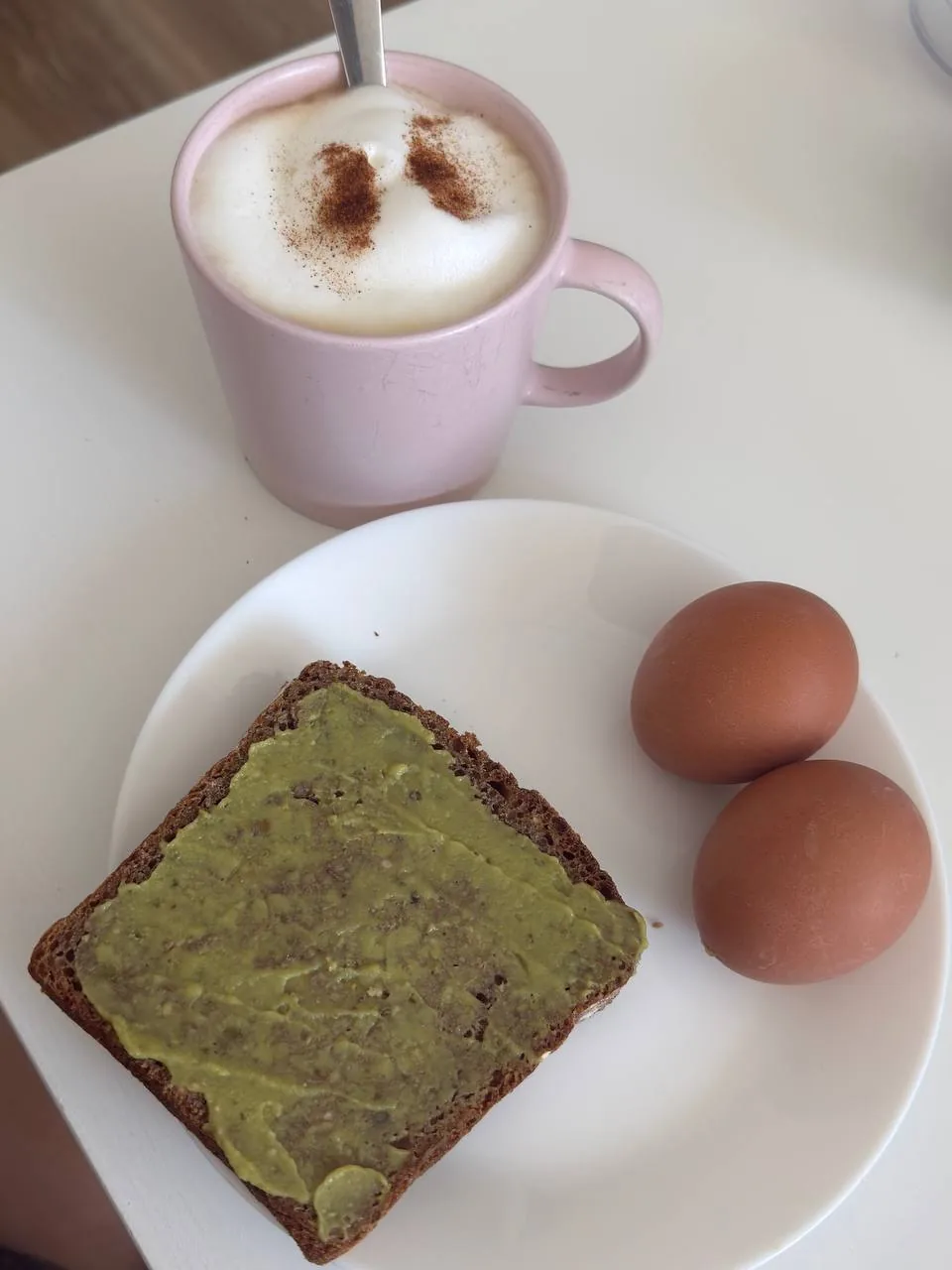 Простой завтрак с напитком, хлебом с зелёной намазкой и двумя яйцами как пример сытного приёма пищи для контроля аппетита