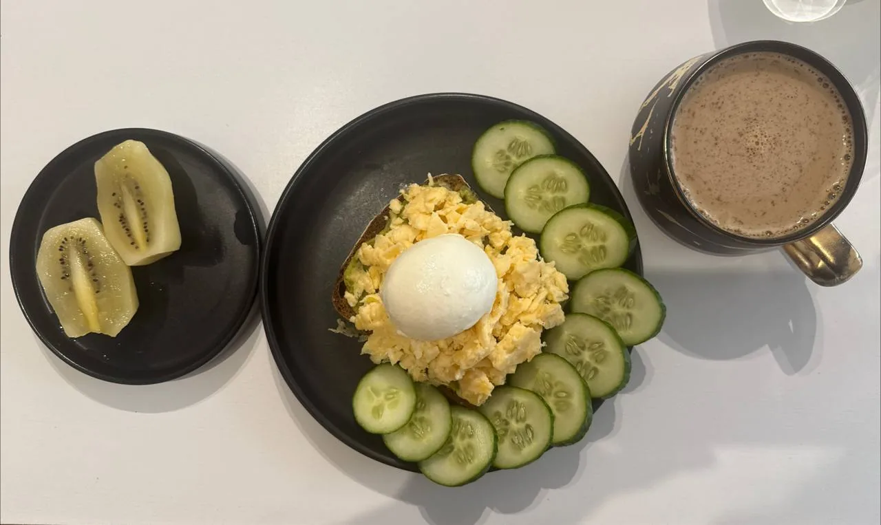 Тарелка с яичницей, тостом, огурцом, фруктами и кофе как пример сытного завтрака для контроля аппетита