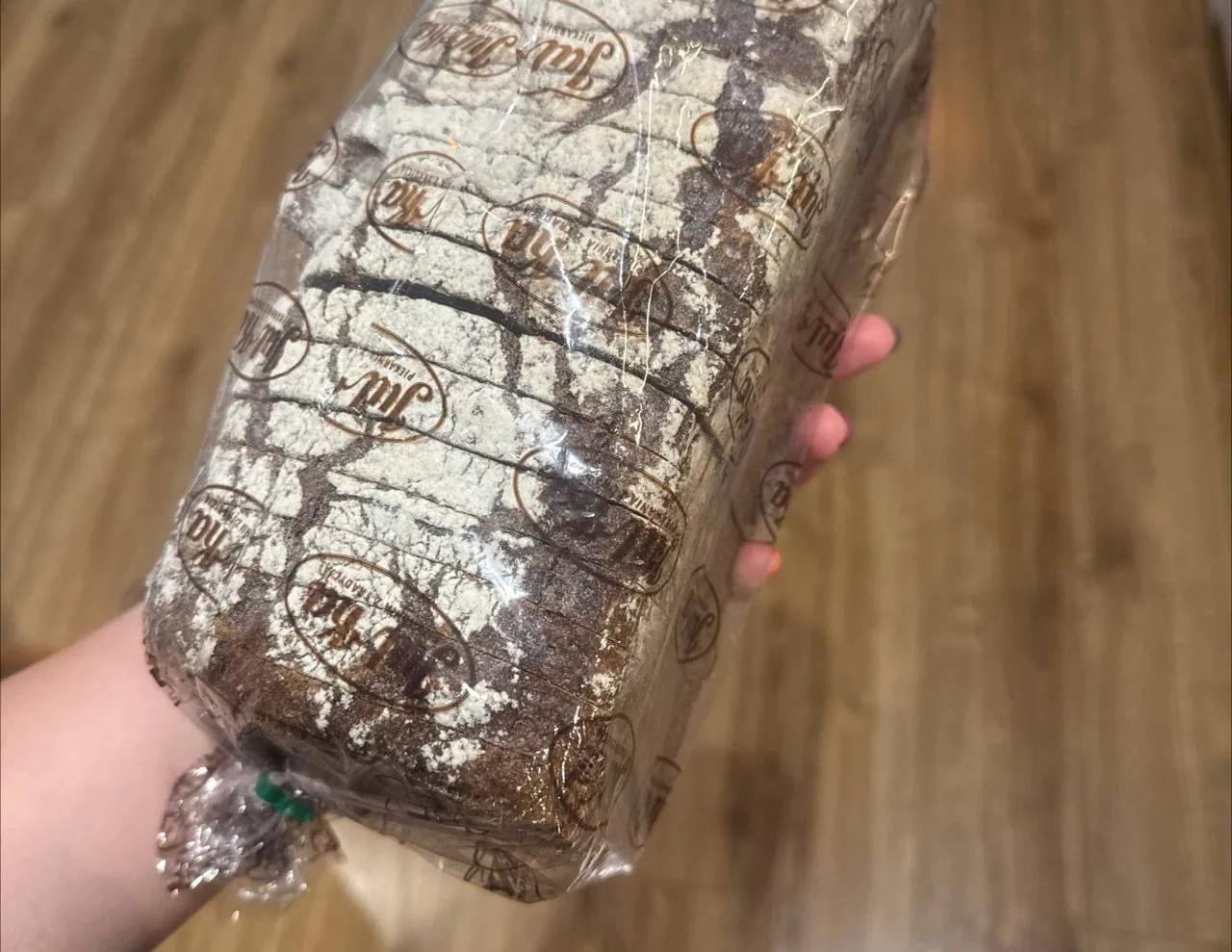 Рука держит буханку хлеба в прозрачной упаковке