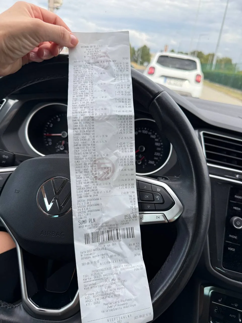 Человек в салоне автомобиля держит длинный чек над рулем, символизируя внимательное отношение к расходам и последствиям терапии