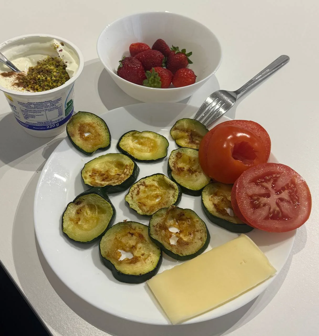 Тарелка с запечёнными цукини, ломтиками помидора, сыром и клубникой рядом с йогуртом — пример более лёгкого приёма пищи при ожирении